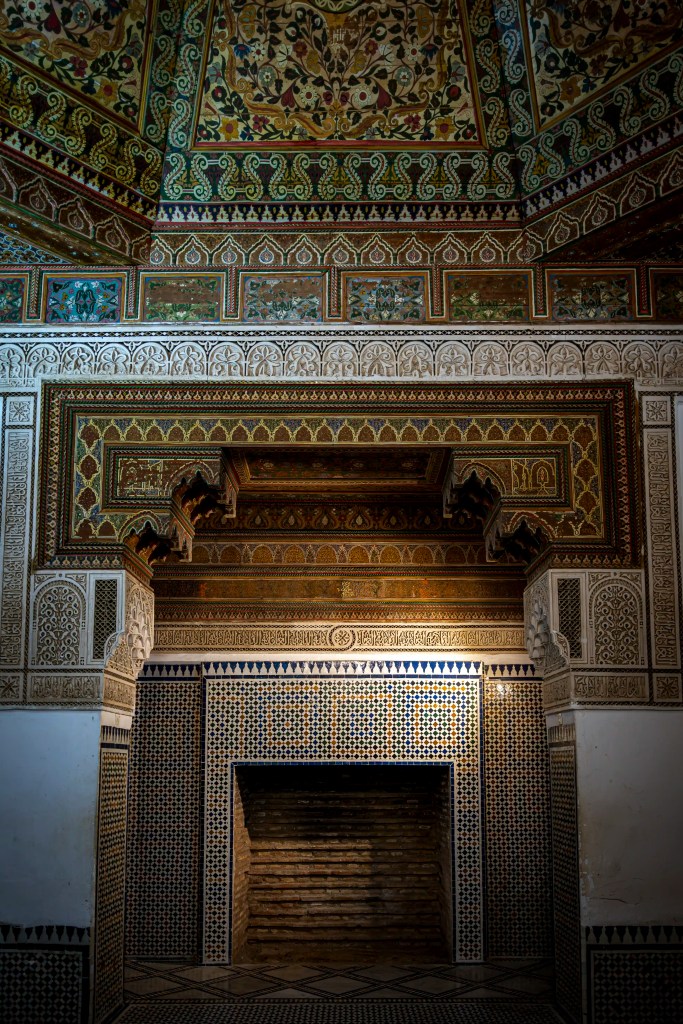 Intricate mural and tile work adorning the walls and ceiling of a traditional Moroccan interior, featuring a decorative fireplace and detailed geometric patterns.